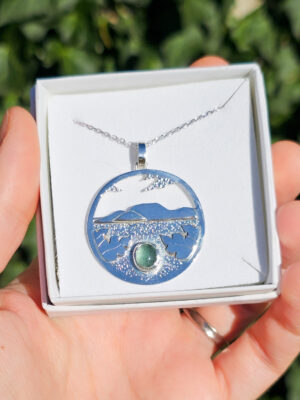 Collier en argent représentant un paysage tanzanien avec des montagnes et des feuilles de bananier, serti d'une tourmaline dichroïque bleue et verte