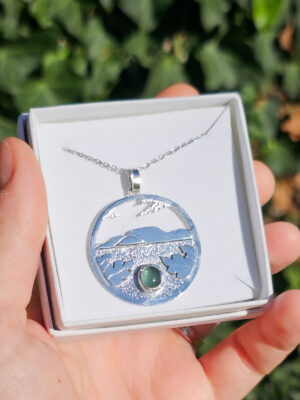 Collier en argent représentant un paysage tanzanien avec des montagnes et des feuilles de bananier, serti d'une tourmaline dichroïque bleue et verte