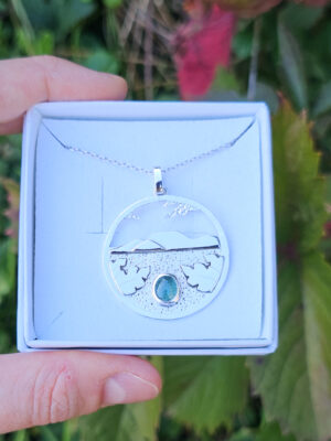 Collier en argent représentant un paysage tanzanien avec des montagnes et des feuilles de bananier, serti d'une tourmaline dichroïque bleue et verte