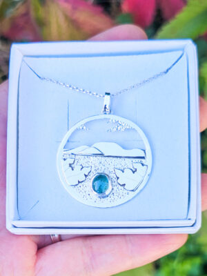 Collier en argent représentant un paysage tanzanien avec des montagnes et des feuilles de bananier, serti d'une tourmaline dichroïque bleue et verte