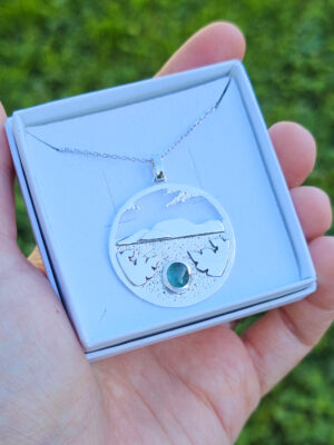 Collier en argent représentant un paysage tanzanien avec des montagnes et des feuilles de bananier, serti d'une tourmaline dichroïque bleue et verte