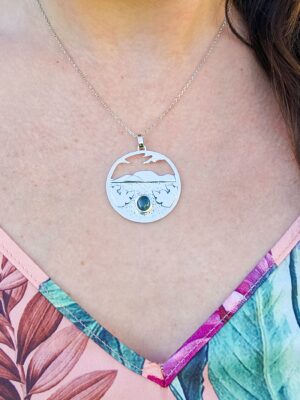 Collier en argent représentant un paysage tanzanien avec des montagnes et des feuilles de bananier, serti d'une tourmaline dichroïque bleue et verte