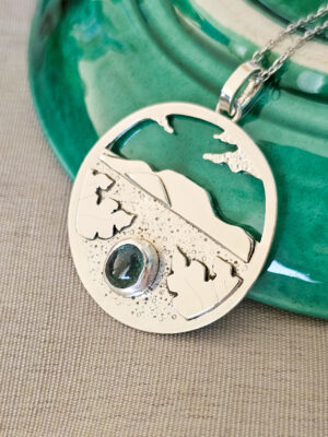 Collier en argent représentant un paysage tanzanien avec des montagnes et des feuilles de bananier, serti d'une tourmaline dichroïque bleue et verte