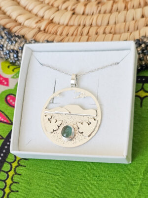 Collier en argent représentant un paysage tanzanien avec des montagnes et des feuilles de bananier, serti d'une tourmaline dichroïque bleue et verte