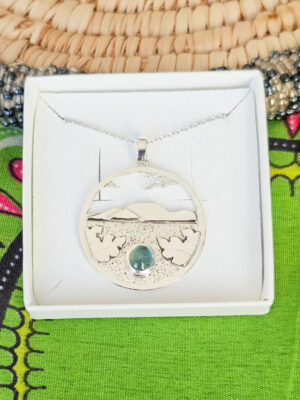 Collier en argent représentant un paysage tanzanien avec des montagnes et des feuilles de bananier, serti d'une tourmaline dichroïque bleue et verte