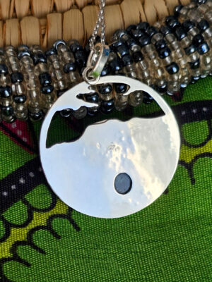 Arrière d'un collier en argent représentant un paysage tanzanien avec des montagnes et des feuilles de bananier, serti d'une tourmaline dichroïque bleue et verte