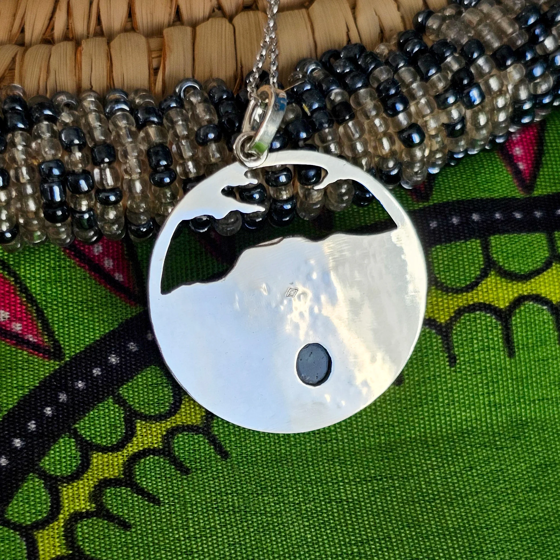Arrière d'un collier en argent représentant un paysage tanzanien avec des montagnes et des feuilles de bananier, serti d'une tourmaline dichroïque bleue et verte
